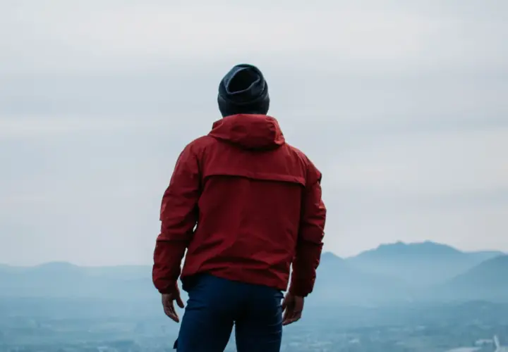 Hombre con chaqueta roja y gorro azul, contemplando el paisaje. ¿Primoloft vs Gore-Tex para esta aventura?