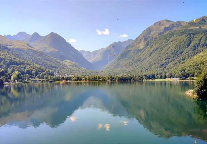 Tranquilo lac de Genos con montañas verdes y paracaidistas en el cielo azul.