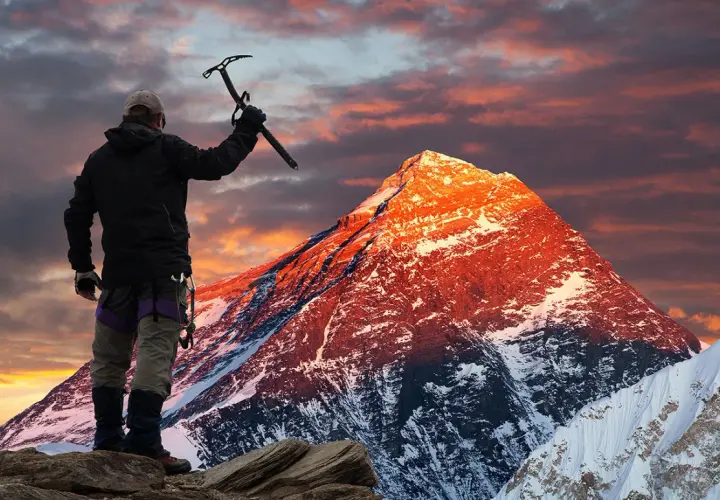 Erik Weihenmayer, escalador, levanta su piolet ante un Everest anaranjado al amanecer.