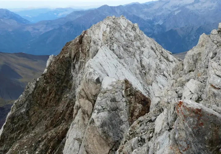 Cresta rocosa y escarpada en el **valle de Vallibierna**, con montañas azules y brumosas al fondo.