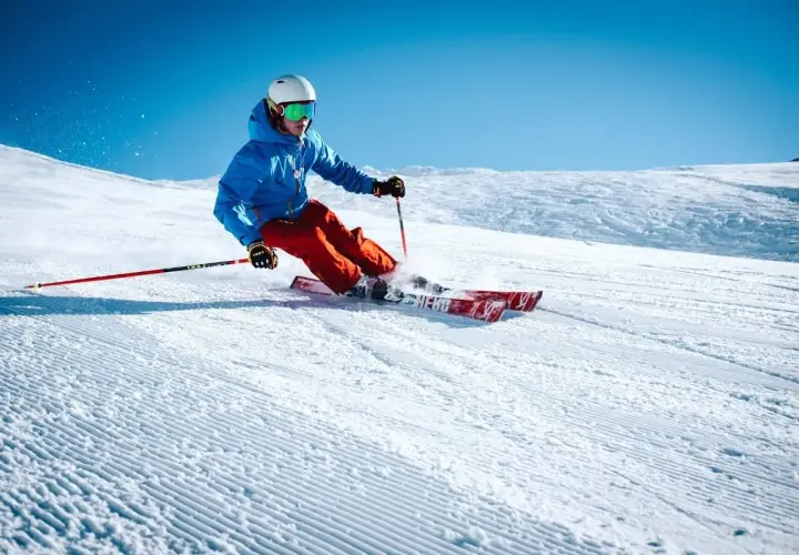 Esquiador con chaqueta azul y pantalones naranjas desciende una pista nevada, demostrando como se esquia con agilidad y estilo.