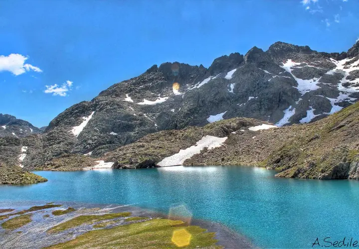 Espectaculares lagos azules en Panticosa, rodeados de montañas rocosas con nieve y un cielo azul intenso.