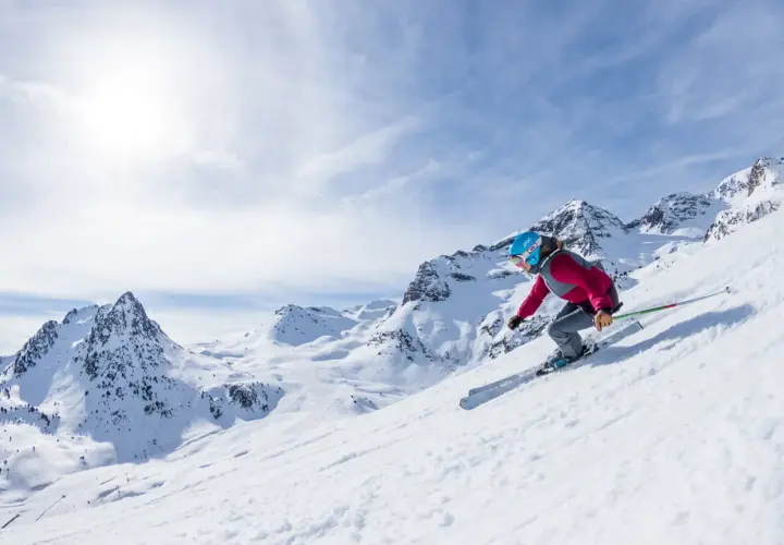 Esquiadora desciende por una ladera nevada en el Pirineo Aragonés, con picos majestuosos de fondo.