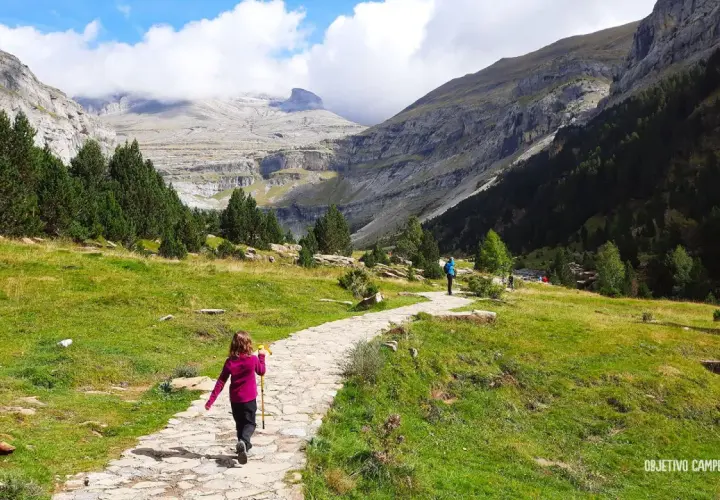 Niños disfrutan de la ruta Cola de Caballo, un camino de piedra serpentea entre prados verdes y montañas imponentes.