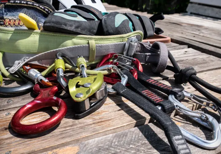Equipo de escalada para rocódromo: arnés, pies de gato, mosquetones, descendedor y cuerda.