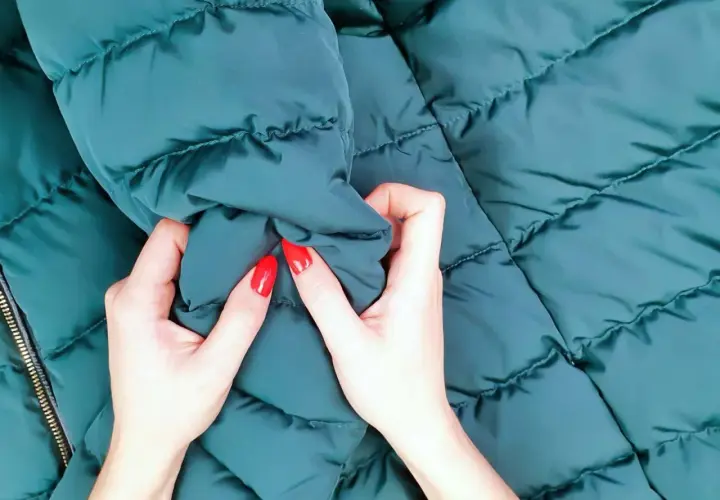 Manos con uñas rojas arrugan una chaqueta verde oscuro recién lavada.
