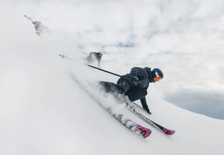 Dos esquiadores disfrutan de un descenso vertiginoso en esqui alpino, levantando nieve en su camino.