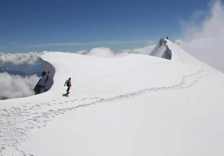 Dani Arnold camina por una cresta nevada, dejando huellas en el camino hacia la cima.