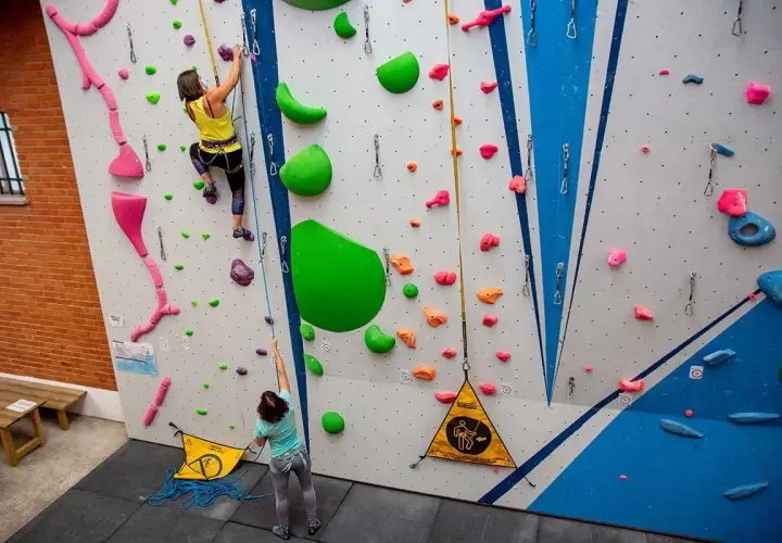 Dos escaladoras practican en un rocódromo, un muro artificial con presas de colores para trepar.