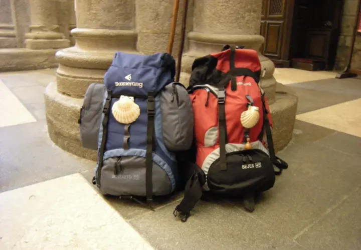 Dos mochilas, una azul y otra roja, con conchas de peregrino, listas para el camino. El tamaño de la mochila es clave para el Camino de Santiago.