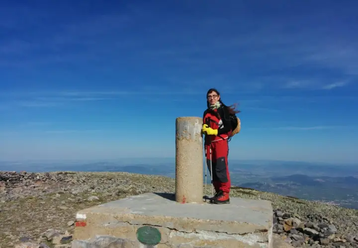 Cumbre del Moncayo, disfrutando de la ruta circular. Una excursionista posa junto al vértice geodésico con bastones de trekking.