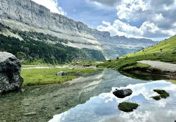 Un lago sereno refleja las imponentes montañas y el cielo nublado en el Parque Nacional de los Pirineos.