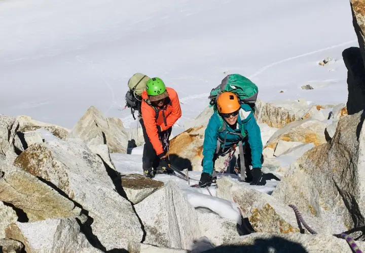 Dos escaladores con mochilas y cascos navegan por rocas y nieve en la montaña. Sus aventuras son como libros abiertos de la naturaleza.