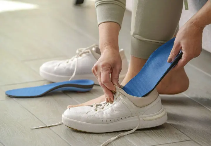 Manos insertando una plantilla azul en una bota blanca. Otra plantilla y una bota están en el suelo.