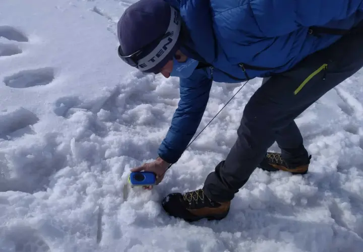Persona en la arva montaña, con equipo de rescate, buscando algo en la nieve.