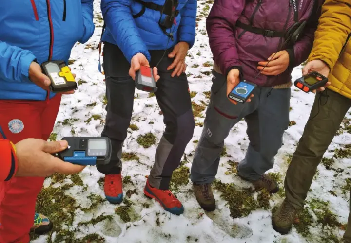 Personas en la nieve sostienen varios dispositivos de búsqueda de avalanchas, como el PIEPS, para una lección de seguridad en montaña.