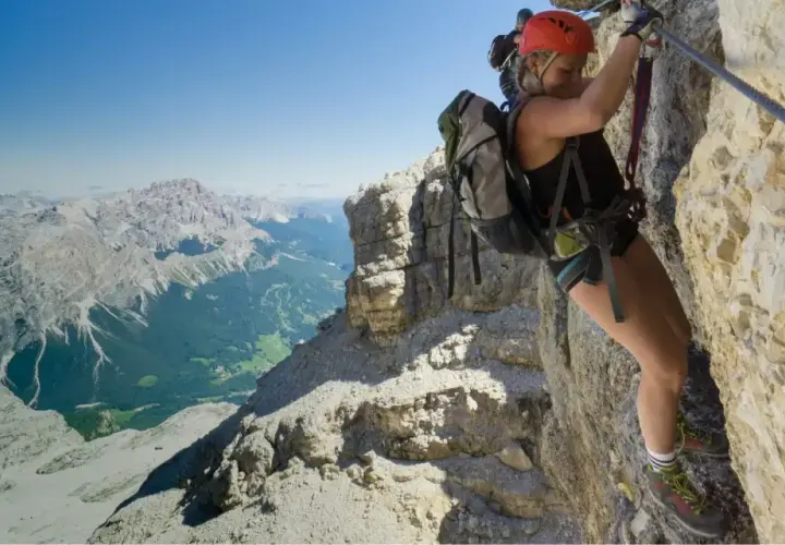 Mujer escalando una vía ferrata en Catalunya, con un paisaje montañoso espectacular de fondo.