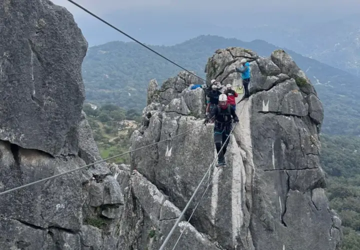 Grupo de personas superando diferentes niveles de vía ferrata, asegurados a cables de acero sobre rocas escarpadas.