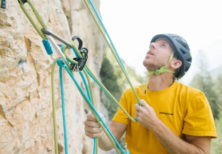 Escalador con casco y camiseta amarilla, asegurando cuerdas de escalada. La **cesta escalada** está lista para la aventura.