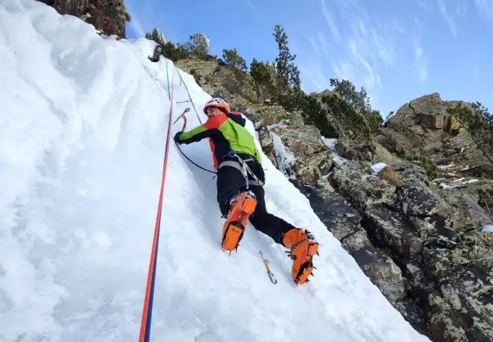 Escalador en hielo en los Pirineos, disfrutando de corredores fáciles con crampones y piolet.
