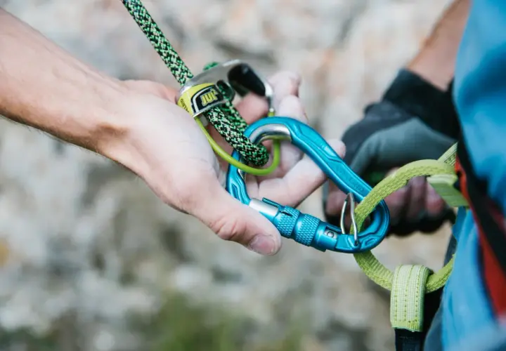 Manos ajustando cuerda y mosquetones azules, esenciales para escalada. Los mejores mosquetones garantizan seguridad.