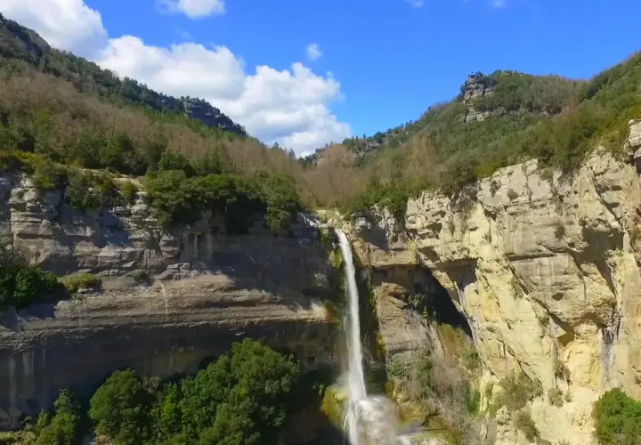 Cascada impresionante en un cañón rocoso, ideal para senderismo en Cataluña. El agua cae en una cortina blanca sobre la piedra dorada.