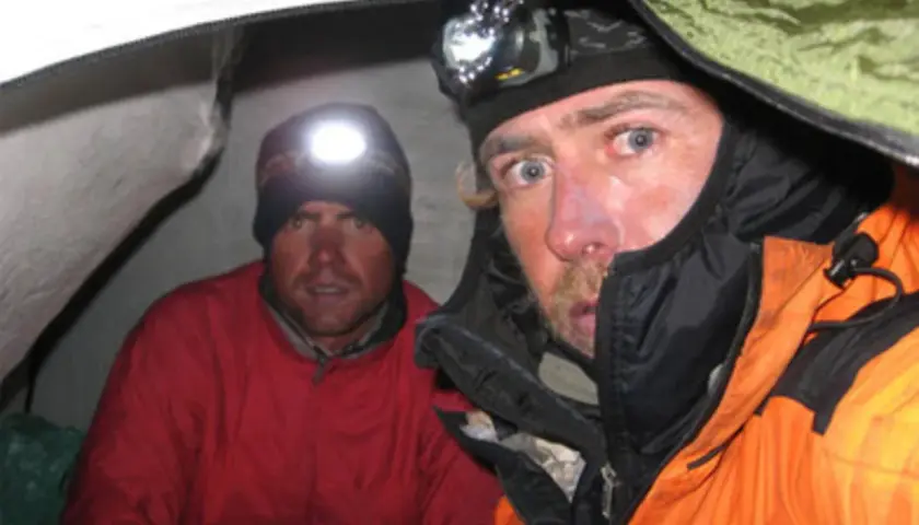 Oscar Pérez, alpinista, y su compañero en una tienda de campaña, ambos con linternas frontales encendidas.