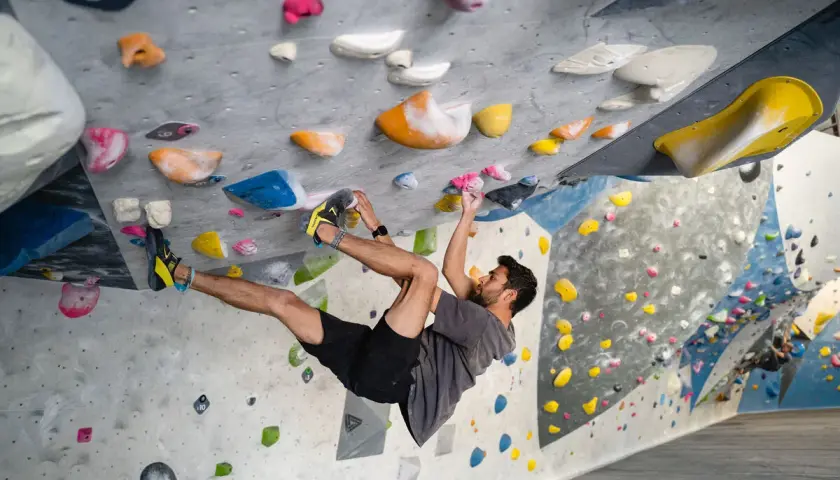 Hombre escalando en un rocódromo interior, superando diferentes grados escalada boulder con agarres de colores.