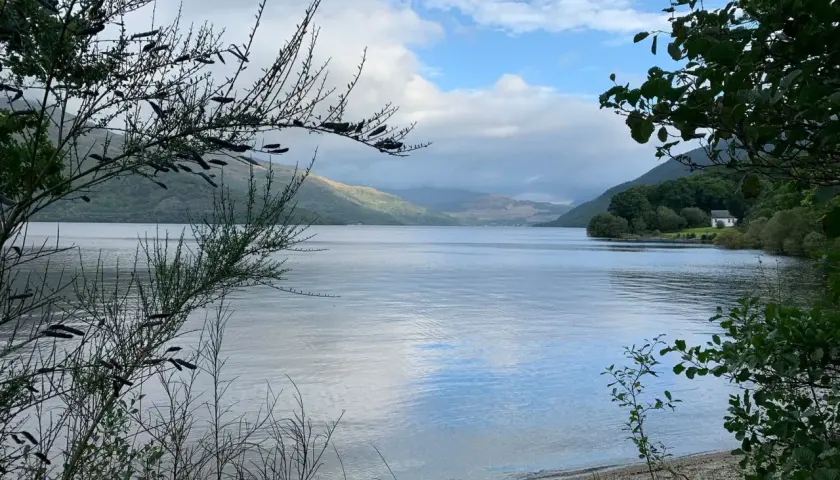 Un lago sereno en el West Highland Way, con colinas cubiertas de vegetación y un cielo nublado.