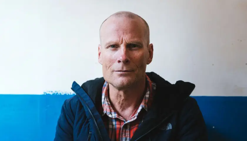 Retrato de Alex Lowe, un hombre calvo con camisa de cuadros y chaqueta azul, mirando fijamente a la cámara.