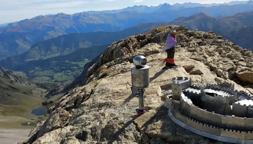 En la cima de una montaña, un monumento con forma de castillo y un poste con una esfera metálica. Al fondo, un valle verde y montañas azules. El **erregeen mahaia** es un lugar de ensueño.