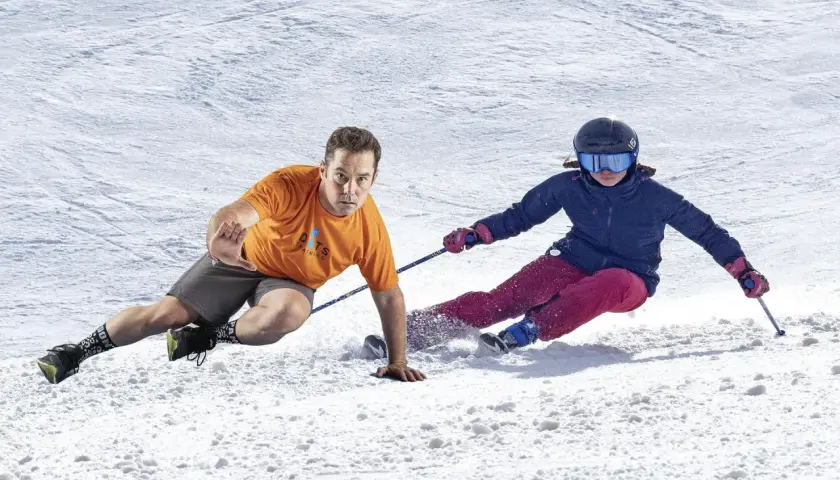 Instructor demuestra ejercicios para esquiar, con un esquiador en la nieve.