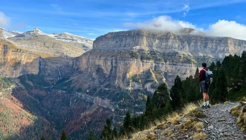 Senderista admira imponentes acantilados y cascadas en las rutas Pirineos. El otoño tiñe el valle de colores cálidos.