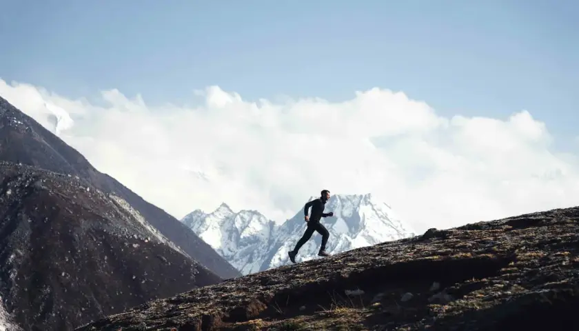 Stephane Brosse corre por una ladera rocosa con picos nevados de fondo.