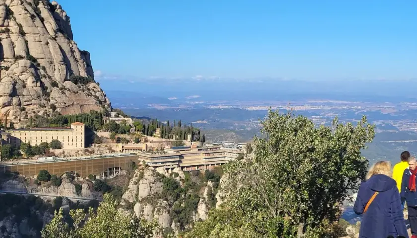 Vista panorámica del monasterio de Sant Miquel de Montserrat, con sus edificios anclados a la montaña y el valle extendiéndose hasta el horizonte.