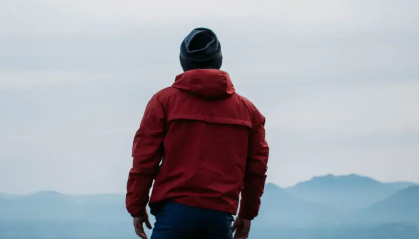 Hombre con chaqueta roja y gorro azul, contemplando el paisaje. ¿Primoloft vs Gore-Tex para esta aventura?