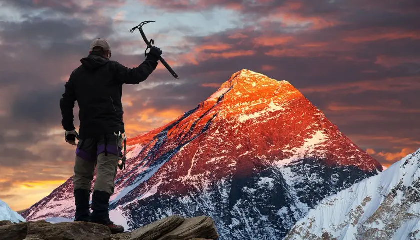 Erik Weihenmayer, escalador, levanta su piolet ante un Everest anaranjado al amanecer.