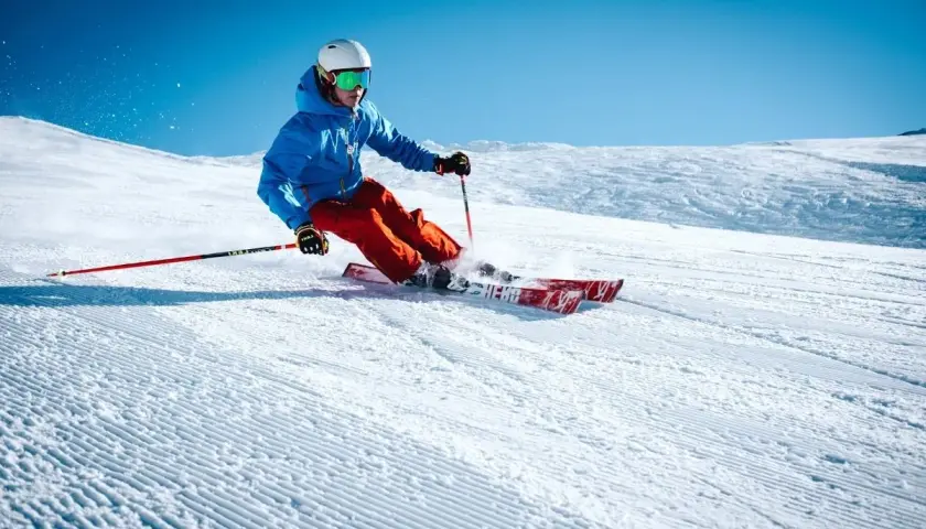 Esquiador con chaqueta azul y pantalones naranjas desciende una pista nevada, demostrando como se esquia con agilidad y estilo.