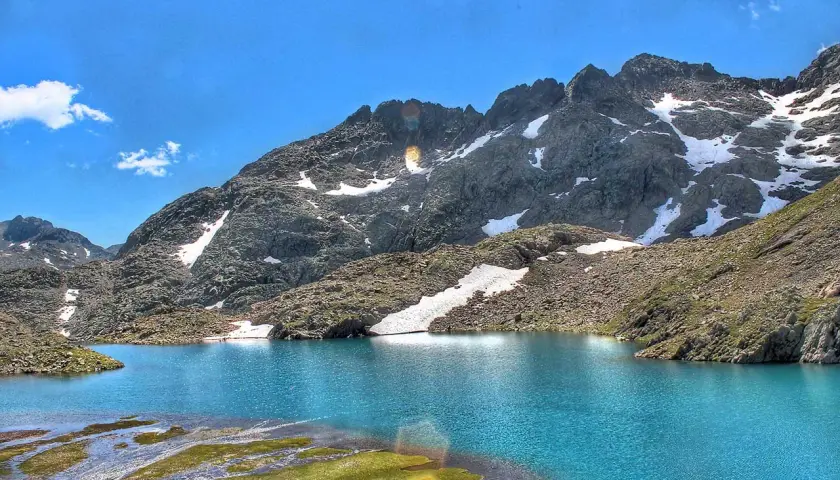 Espectaculares lagos azules en Panticosa, rodeados de montañas rocosas con nieve y un cielo azul intenso.