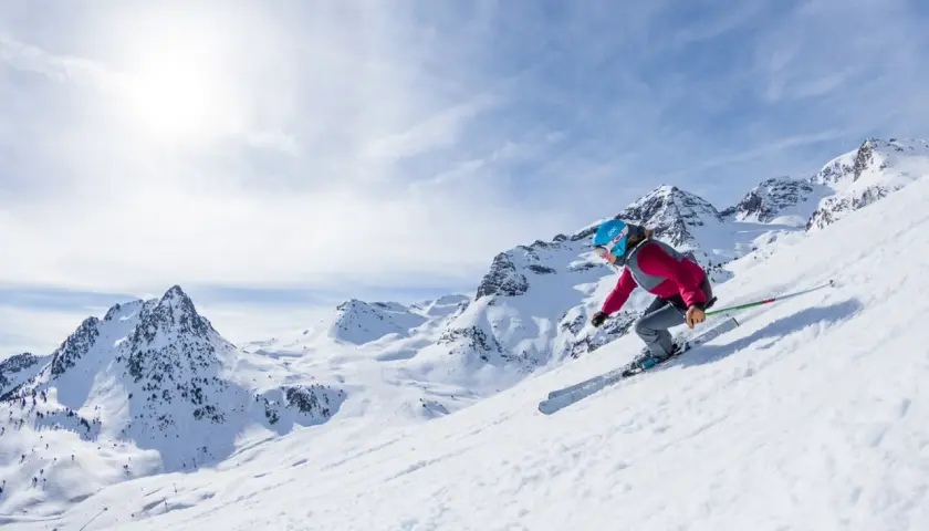Esquiadora desciende por una ladera nevada en el Pirineo Aragonés, con picos majestuosos de fondo.