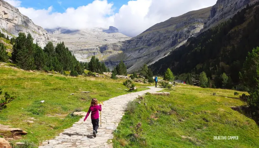 Niños disfrutan de la ruta Cola de Caballo, un camino de piedra serpentea entre prados verdes y montañas imponentes.
