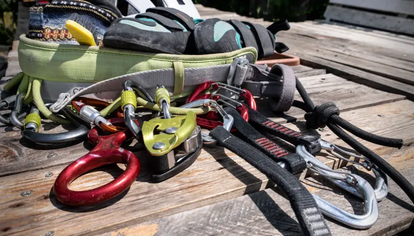 Equipo de escalada para rocódromo: arnés, pies de gato, mosquetones, descendedor y cuerda.
