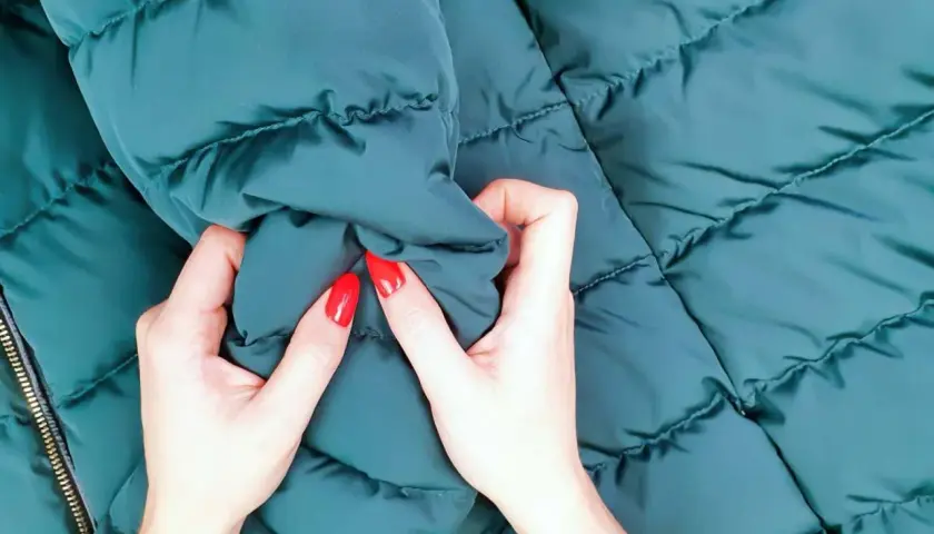 Manos con uñas rojas arrugan una chaqueta verde oscuro recién lavada.