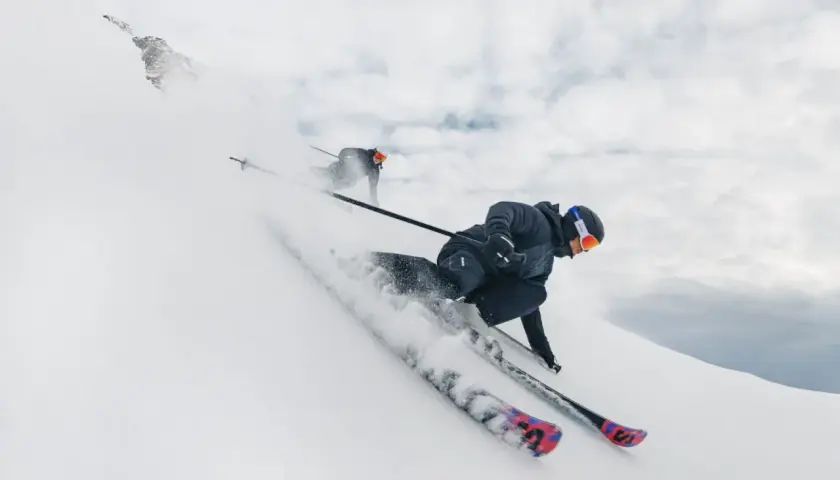 Dos esquiadores disfrutan de un descenso vertiginoso en esqui alpino, levantando nieve en su camino.