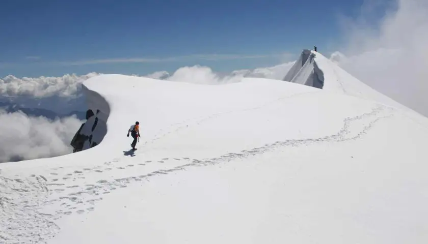 Dani Arnold camina por una cresta nevada, dejando huellas en el camino hacia la cima.