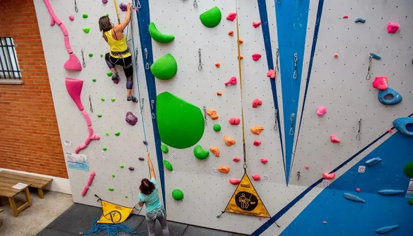 Dos escaladoras practican en un rocódromo, un muro artificial con presas de colores para trepar.