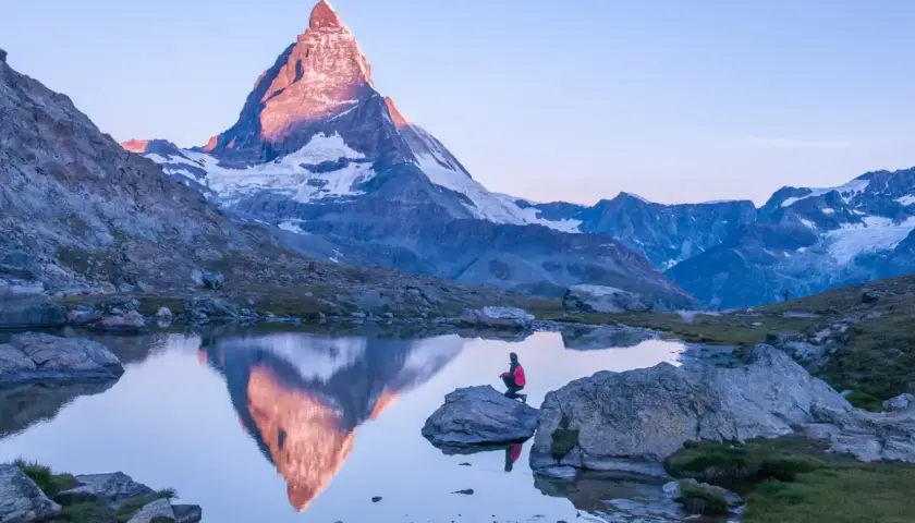 Persona sentada en roca junto a lago, contemplando el reflejo del **Cervino** al amanecer.