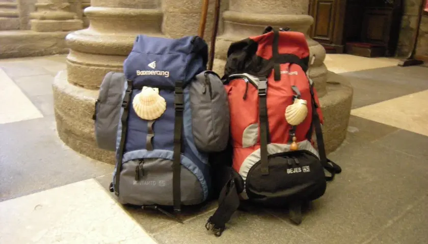 Dos mochilas, una azul y otra roja, con conchas de peregrino, listas para el camino. El tamaño de la mochila es clave para el Camino de Santiago.