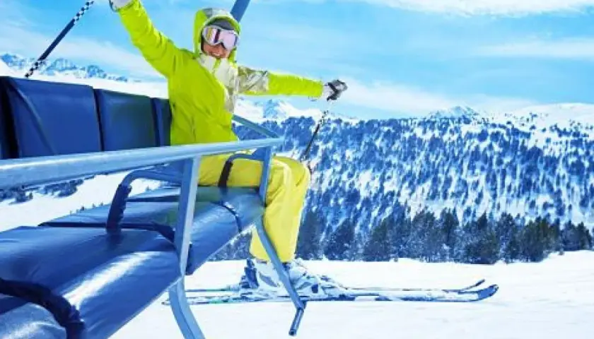 Mujer emocionada en telesilla, lista para hacer sky en la montaña nevada.
