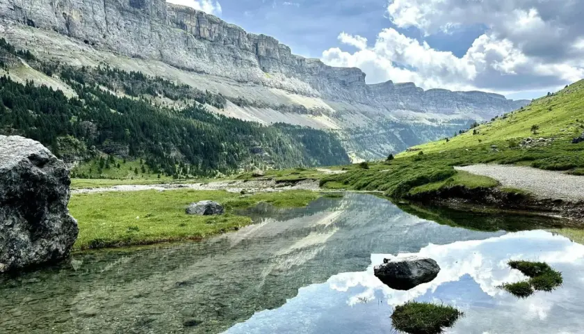 Un lago sereno refleja las imponentes montañas y el cielo nublado en el Parque Nacional de los Pirineos.